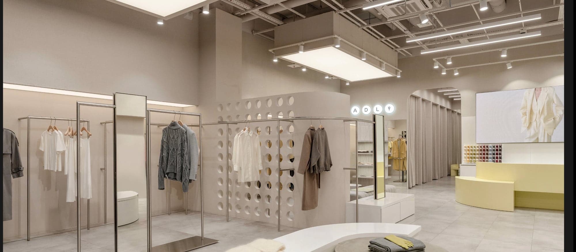 Vue panoramique de la boutique ADL avec banquettes courbes jaunes, écran central et portants inox